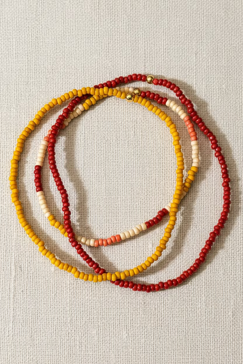 Three beaded bracelets  in red, yellow, and white on a linen surface