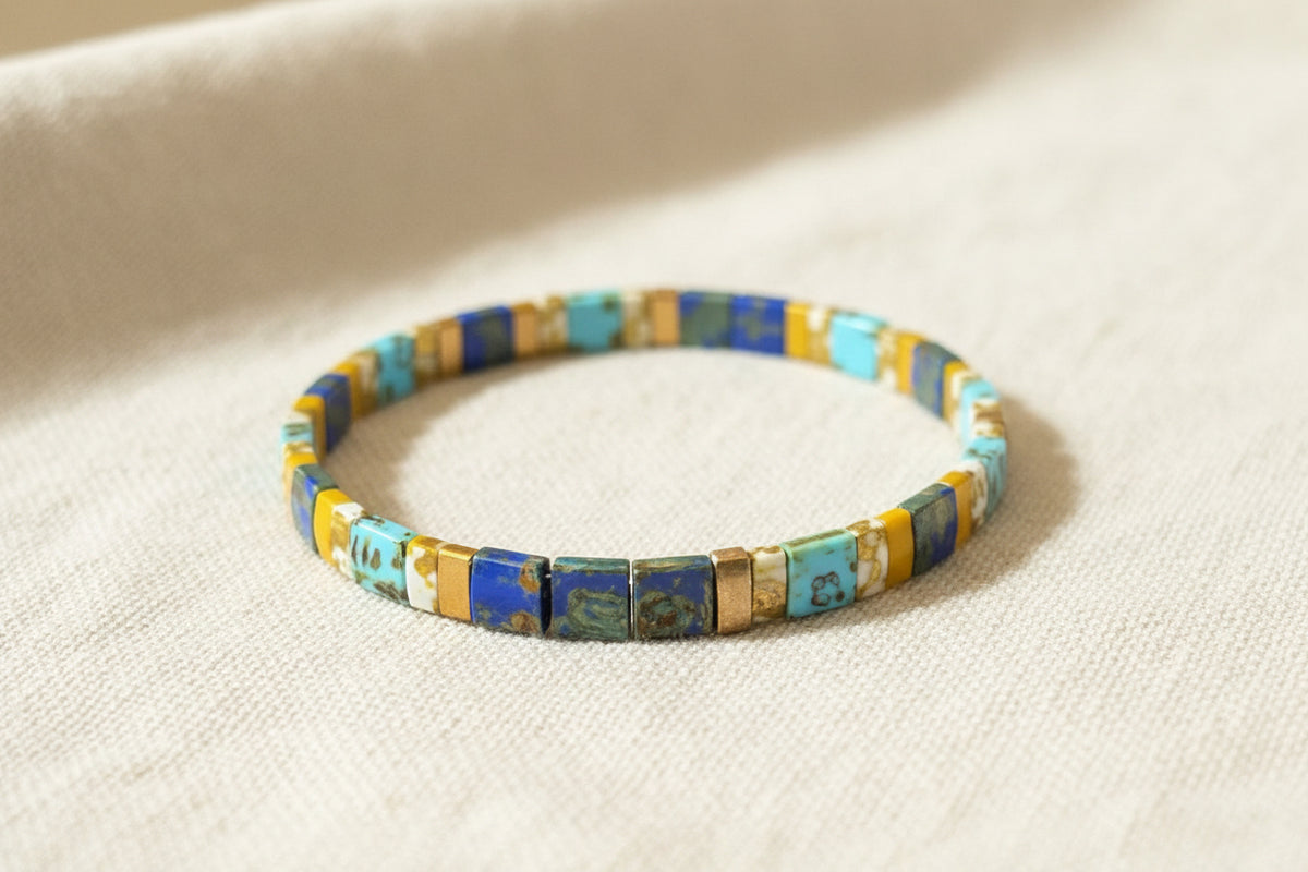 A clear plastic bangle bracelet featuring a colorful mosaic of rectangular beads in blue, turquoise, yellow, and brown, resting on a dark wooden surface.